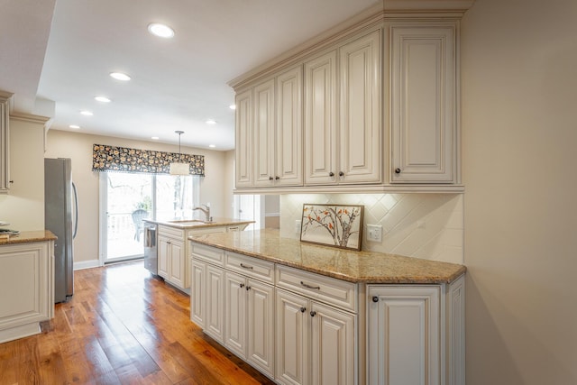 kitchen with light hardwood / wood-style flooring, appliances with stainless steel finishes, pendant lighting, light stone countertops, and cream cabinetry