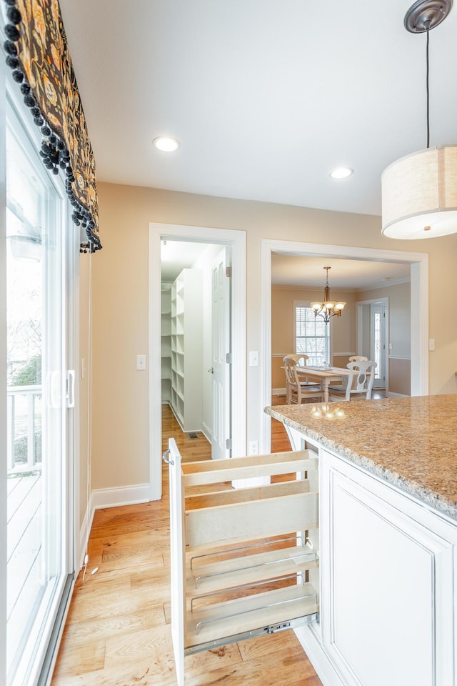 interior space featuring white cabinets, hanging light fixtures, a notable chandelier, light stone counters, and light wood-type flooring