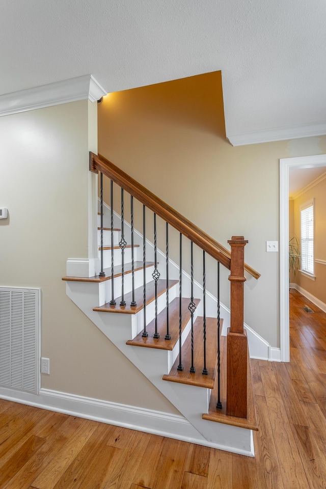 staircase featuring hardwood / wood-style flooring, ornamental molding, and a textured ceiling