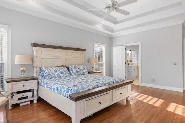 bedroom featuring dark wood-type flooring, ensuite bathroom, ornamental molding, a raised ceiling, and ceiling fan