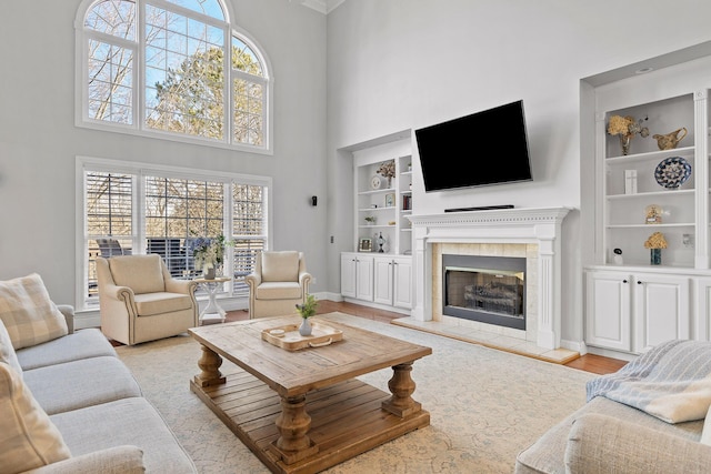 living room featuring a tiled fireplace, a towering ceiling, light hardwood / wood-style flooring, and built in features