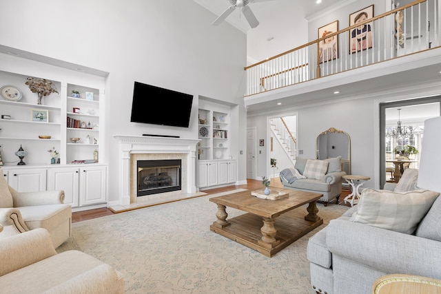 living room featuring crown molding, ceiling fan with notable chandelier, built in features, and light hardwood / wood-style flooring