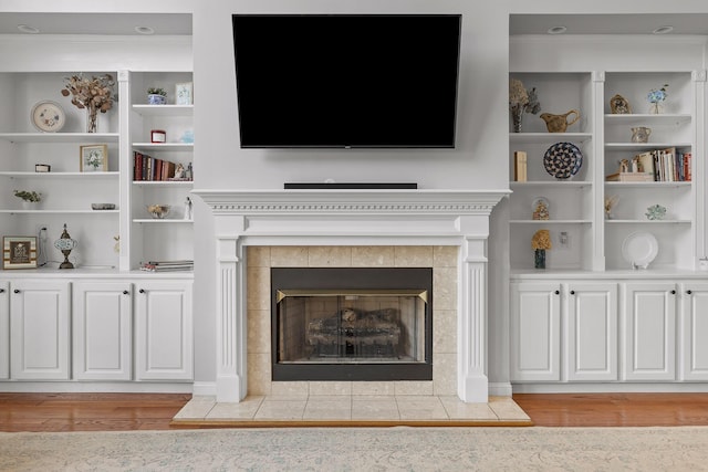 details with a tiled fireplace, built in shelves, and wood-type flooring