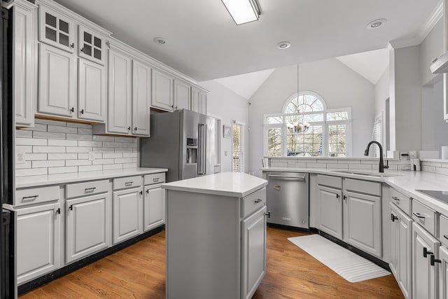 kitchen with sink, vaulted ceiling, a kitchen island, stainless steel appliances, and decorative backsplash