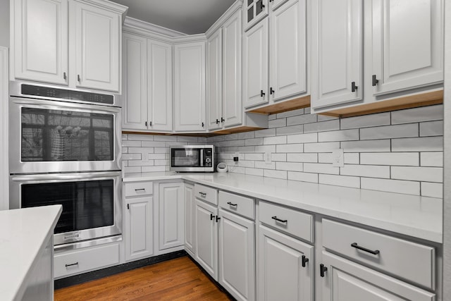 kitchen with tasteful backsplash, dark hardwood / wood-style floors, stainless steel double oven, and white cabinets