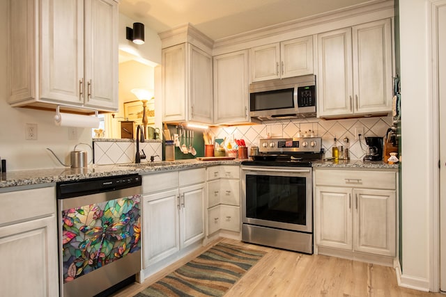 kitchen with sink, light hardwood / wood-style flooring, appliances with stainless steel finishes, backsplash, and light stone counters