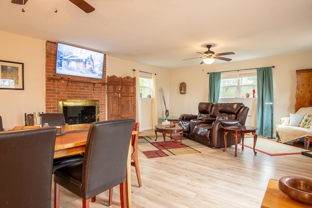 living room with ceiling fan, a brick fireplace, and light wood-type flooring