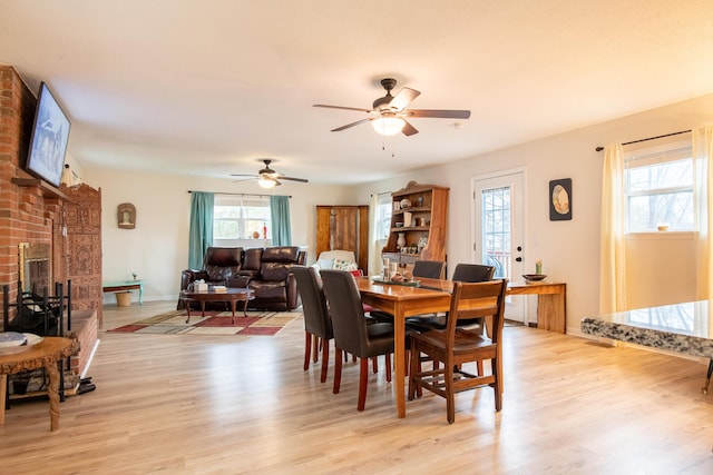 dining area with a healthy amount of sunlight, a brick fireplace, and light hardwood / wood-style flooring