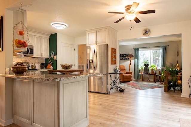 kitchen with white cabinetry, light stone counters, kitchen peninsula, stainless steel appliances, and light wood-type flooring