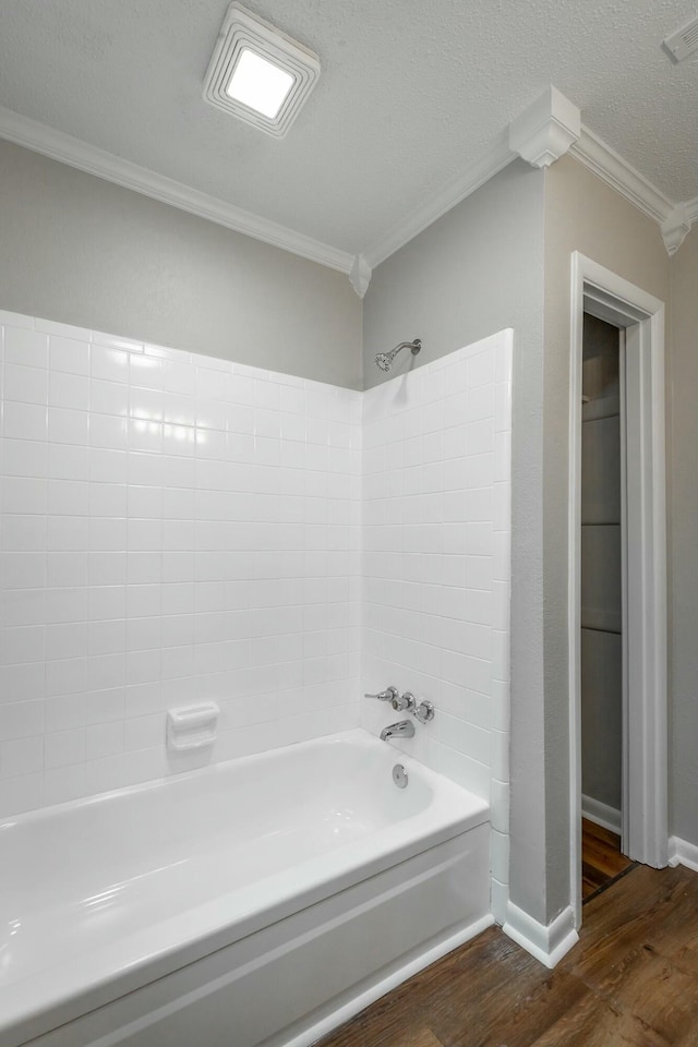 bathroom with hardwood / wood-style flooring, ornamental molding, bathing tub / shower combination, and a textured ceiling