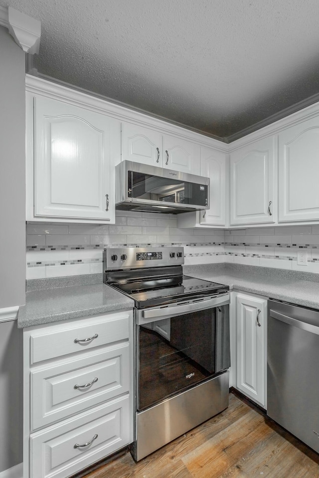 kitchen with decorative backsplash, light hardwood / wood-style flooring, white cabinets, and appliances with stainless steel finishes