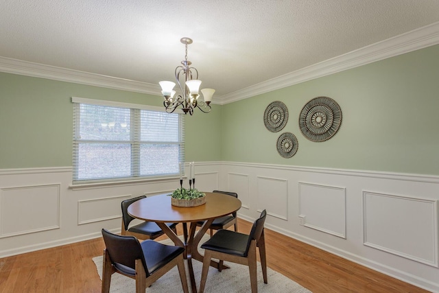 dining area with a textured ceiling, ornamental molding, light hardwood / wood-style floors, and a chandelier