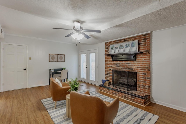 living room featuring wood-type flooring, ornamental molding, a brick fireplace, a textured ceiling, and french doors