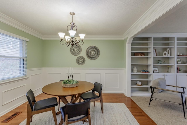 dining room featuring wood-type flooring, a textured ceiling, ornamental molding, built in features, and a notable chandelier