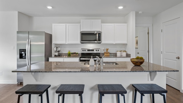 kitchen featuring sink, dark stone countertops, stainless steel appliances, an island with sink, and white cabinets