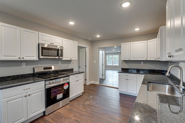 kitchen featuring appliances with stainless steel finishes, white cabinetry, sink, dark stone counters, and dark wood-type flooring