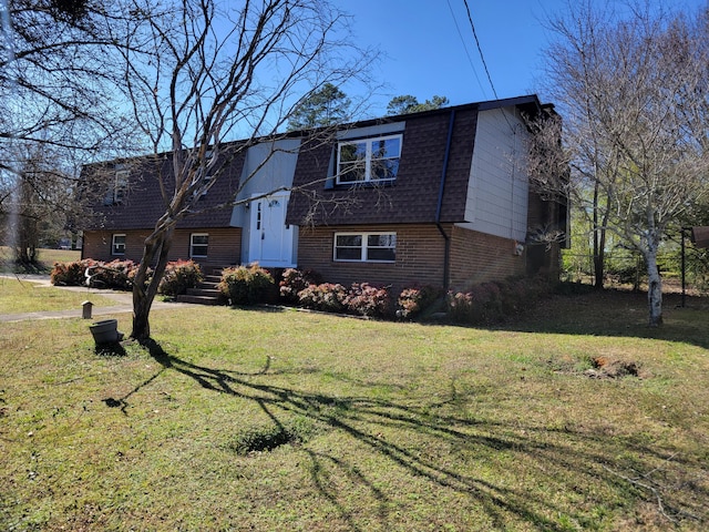 view of front of house with a shingled roof, brick siding, and a front lawn