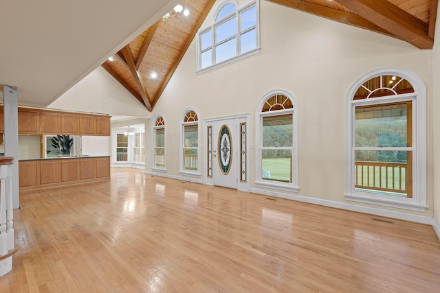 unfurnished living room featuring a wealth of natural light, light hardwood / wood-style flooring, wooden ceiling, and beamed ceiling