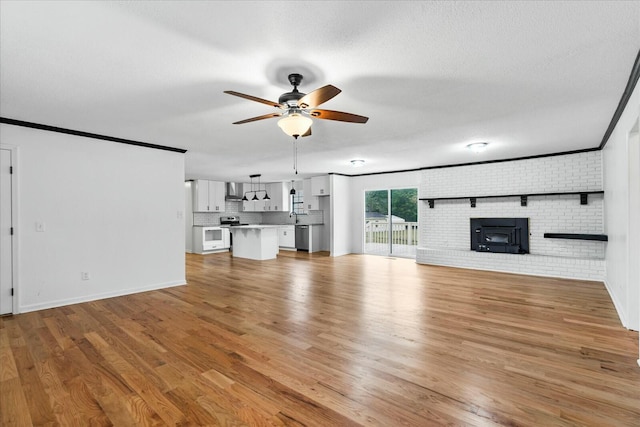 unfurnished living room featuring crown molding, ceiling fan, a textured ceiling, brick wall, and light wood-type flooring