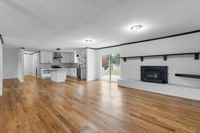 unfurnished living room with brick wall, sink, light hardwood / wood-style floors, and a textured ceiling