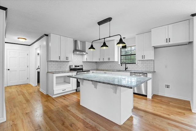 kitchen featuring white cabinetry, stainless steel appliances, a kitchen island, and wall chimney range hood