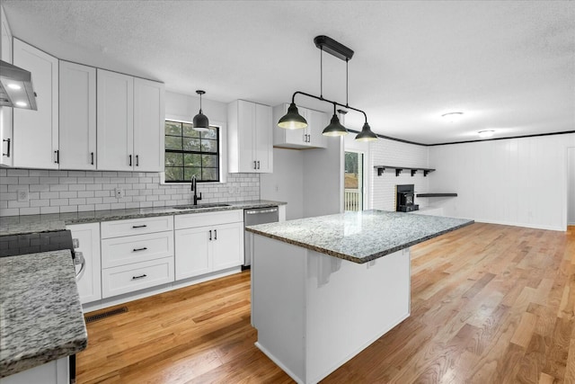 kitchen featuring sink, light stone counters, white cabinets, decorative light fixtures, and stainless steel dishwasher