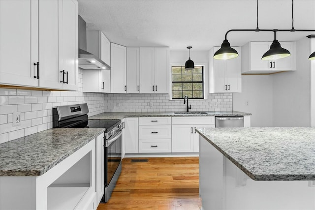 kitchen with sink, white cabinetry, stainless steel appliances, decorative light fixtures, and wall chimney exhaust hood