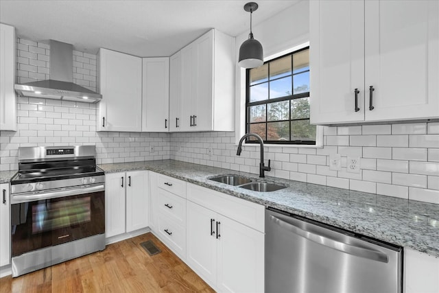 kitchen featuring appliances with stainless steel finishes, pendant lighting, sink, white cabinets, and wall chimney range hood