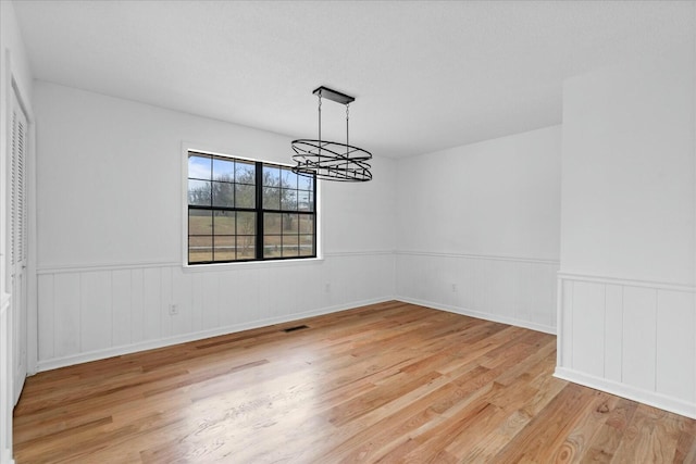 unfurnished dining area with an inviting chandelier and light wood-type flooring