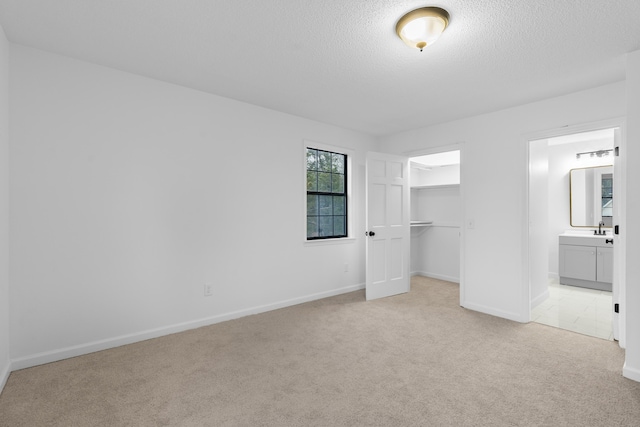 unfurnished bedroom with ensuite bathroom, a walk in closet, light colored carpet, a textured ceiling, and a closet