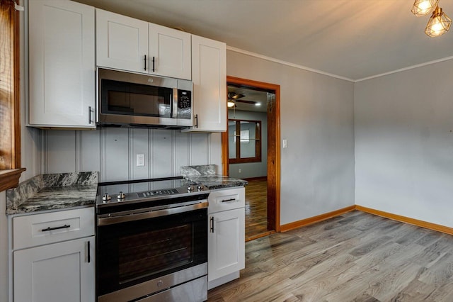 kitchen with appliances with stainless steel finishes, dark stone countertops, ornamental molding, light hardwood / wood-style floors, and white cabinets