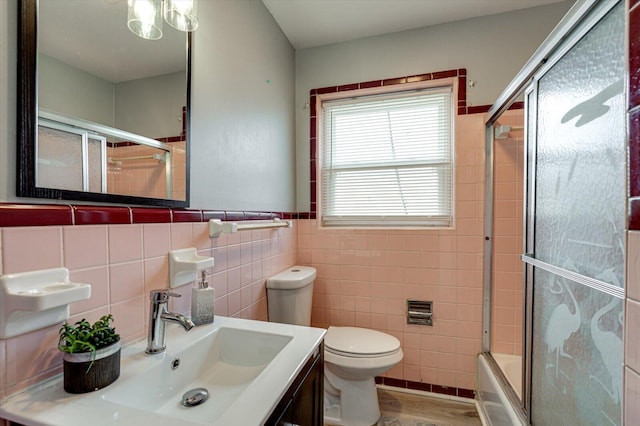 full bathroom with combined bath / shower with glass door, hardwood / wood-style floors, tile walls, vanity, and toilet