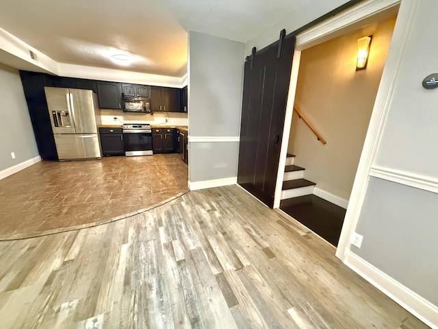 kitchen featuring a barn door, appliances with stainless steel finishes, light wood-type flooring, and dark brown cabinetry