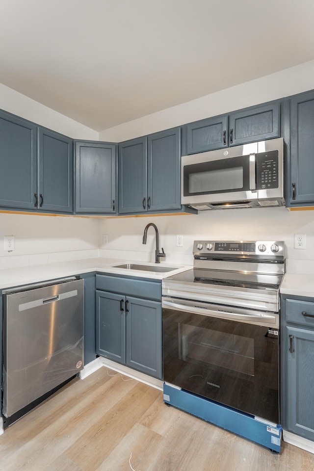 kitchen with appliances with stainless steel finishes, light hardwood / wood-style floors, sink, and blue cabinets