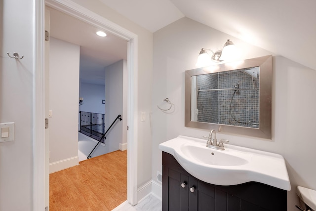 full bath featuring a tile shower, vanity, baseboards, and vaulted ceiling