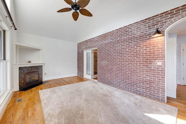 unfurnished living room featuring a tiled fireplace, brick wall, ceiling fan, and wood finished floors