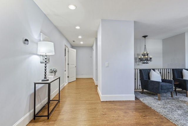 hall featuring baseboards, light wood-type flooring, and an inviting chandelier