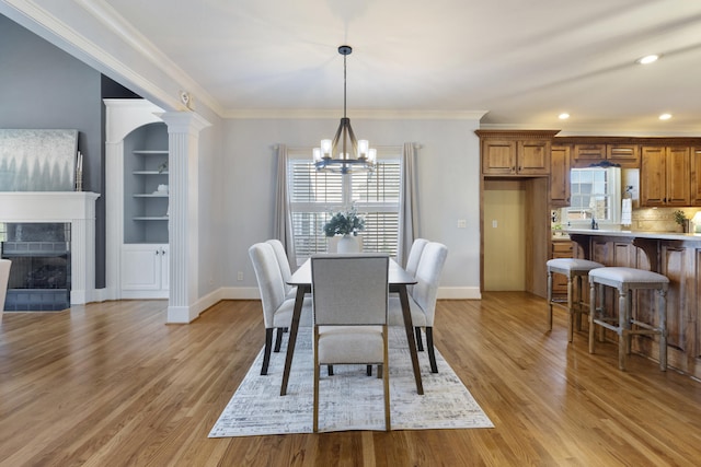 dining room featuring baseboards, a chandelier, ornamental molding, light wood-style flooring, and a fireplace