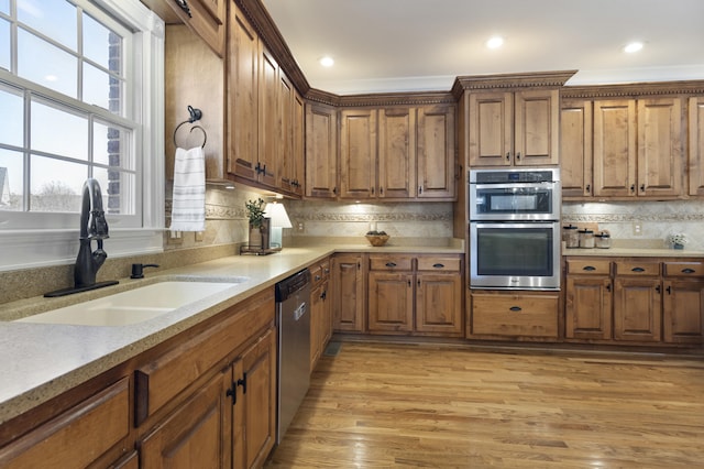 kitchen with brown cabinets, light wood-style flooring, a sink, stainless steel appliances, and decorative backsplash