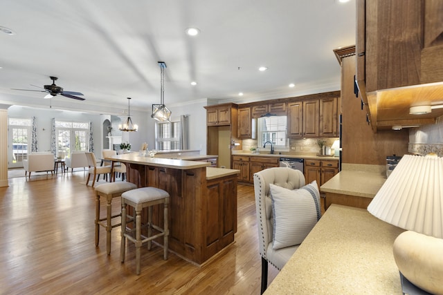 kitchen with a kitchen bar, light wood-style flooring, ceiling fan with notable chandelier, backsplash, and light countertops
