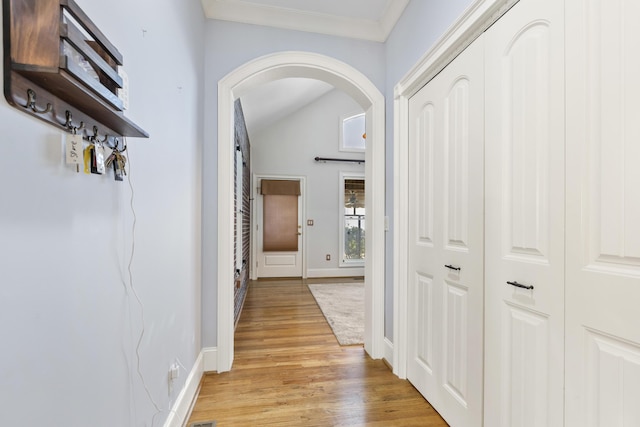 hallway featuring crown molding, baseboards, arched walkways, and light wood finished floors