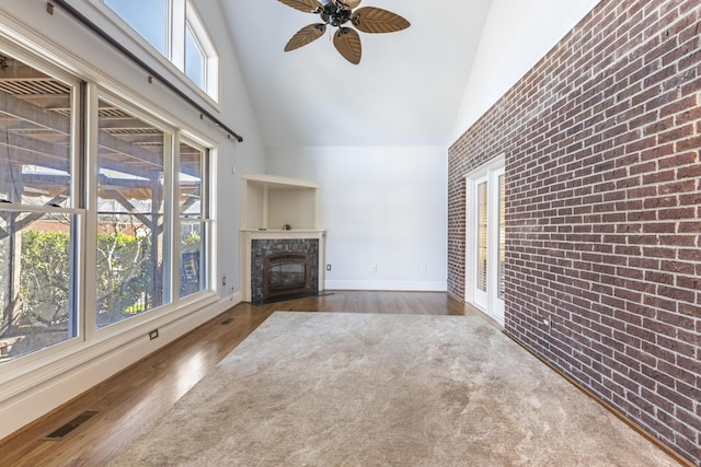 unfurnished living room featuring wood finished floors, visible vents, brick wall, high vaulted ceiling, and a tiled fireplace