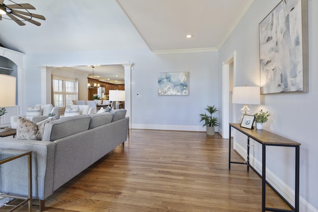 living room featuring wood finished floors, ceiling fan with notable chandelier, ornate columns, and ornamental molding