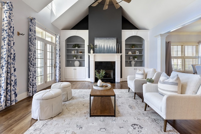 living room featuring a fireplace with flush hearth, built in shelves, a ceiling fan, wood finished floors, and baseboards