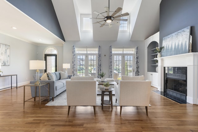 living area with built in shelves, a fireplace, ceiling fan, and wood finished floors