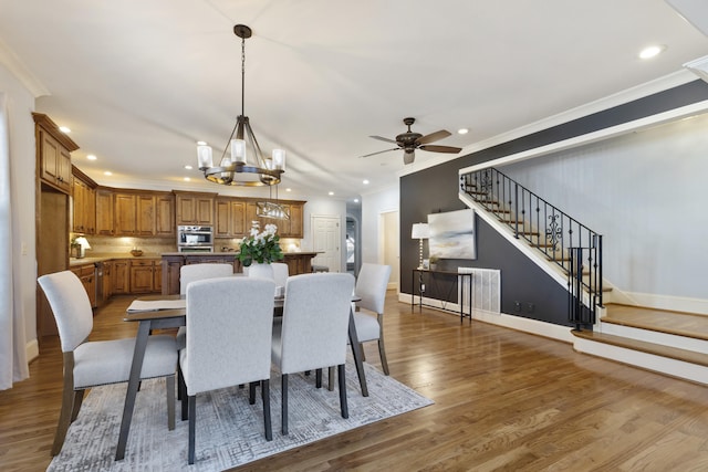 dining area with crown molding, baseboards, stairs, ceiling fan with notable chandelier, and wood finished floors