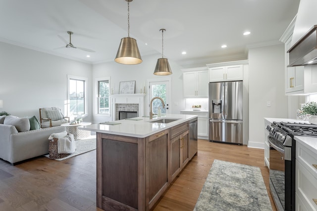 kitchen with sink, stainless steel appliances, wood-type flooring, white cabinets, and a center island with sink