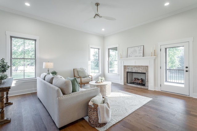 living room with ceiling fan, ornamental molding, wood-type flooring, and a brick fireplace