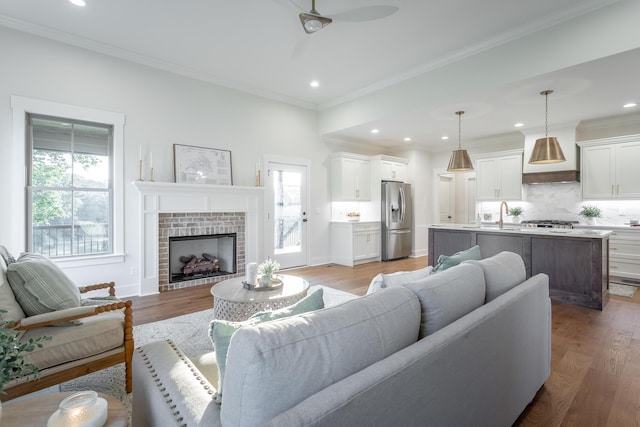 living room with sink, ceiling fan, a fireplace, ornamental molding, and light wood-type flooring