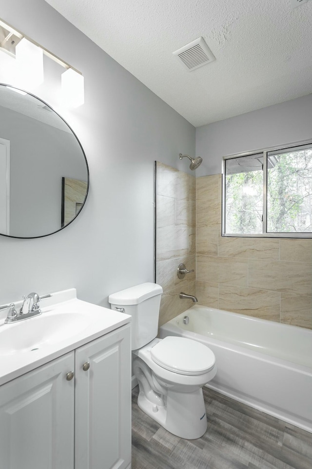 full bathroom featuring tiled shower / bath combo, vanity, hardwood / wood-style flooring, toilet, and a textured ceiling